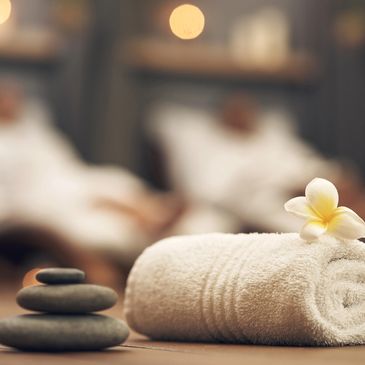 Spa setting with rolled towel, flower, and stacked stones.