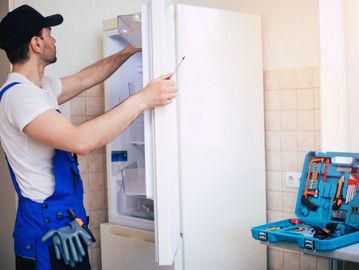 Technician inspecting a refrigerator with tools laid out nearby.
