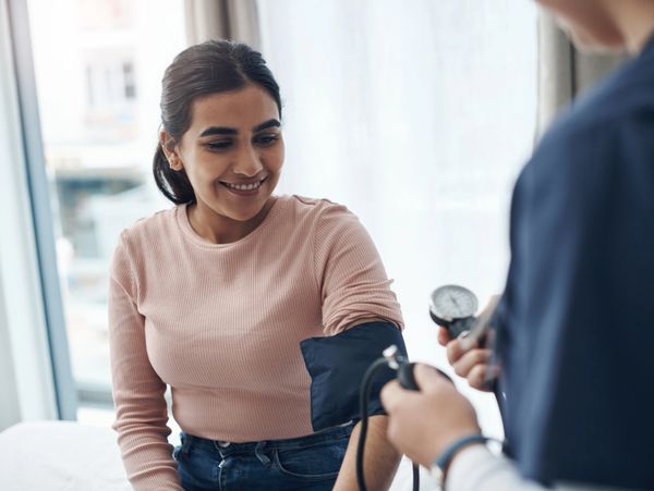 A woman smiling while getting her blood pressure checked by a healthcare professional.