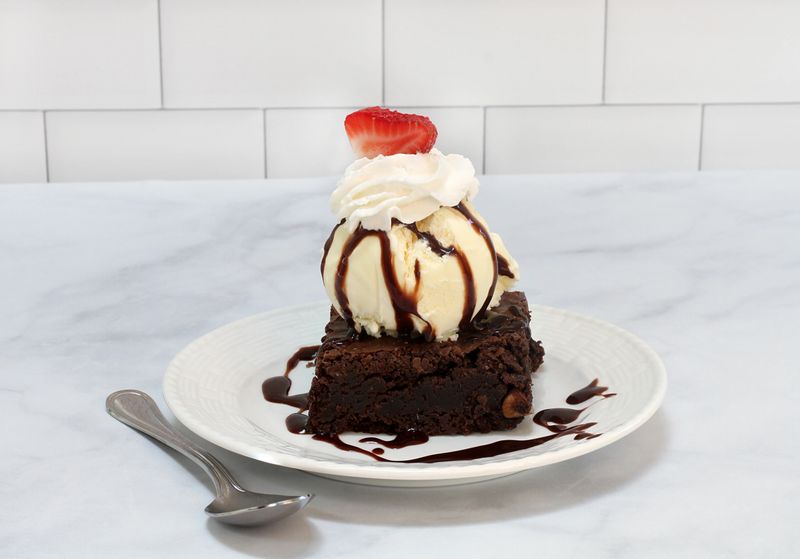 Brownie Ice Cream Sundae with vanilla ice cream and topped with chocolate sauce and a slice of strawberry.
