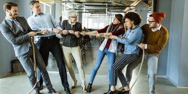 Two teams in office playing tug of war, showing teamwork and competition.