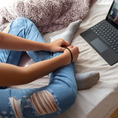 Person sitting cross-legged on bed next to laptop.