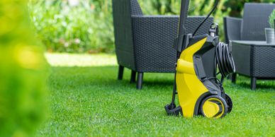 Yellow pressure washer on green grass near outdoor chairs.