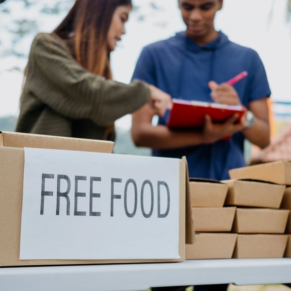 Volunteers distributing free food in cardboard boxes at an outdoor event.
