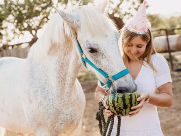 Girl feeding watermelon to a white horse.