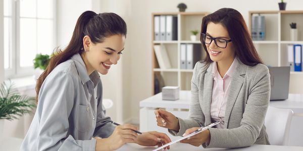 Two women smiling and discussing documents in a bright office.