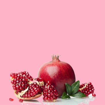 Whole and sliced pomegranate with seeds on a pink background.