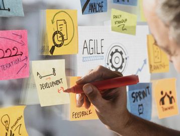 Person marking a sticky note with development notes during agile planning.