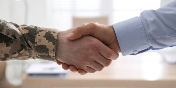 A handshake between a person in military uniform and a person in business attire.
