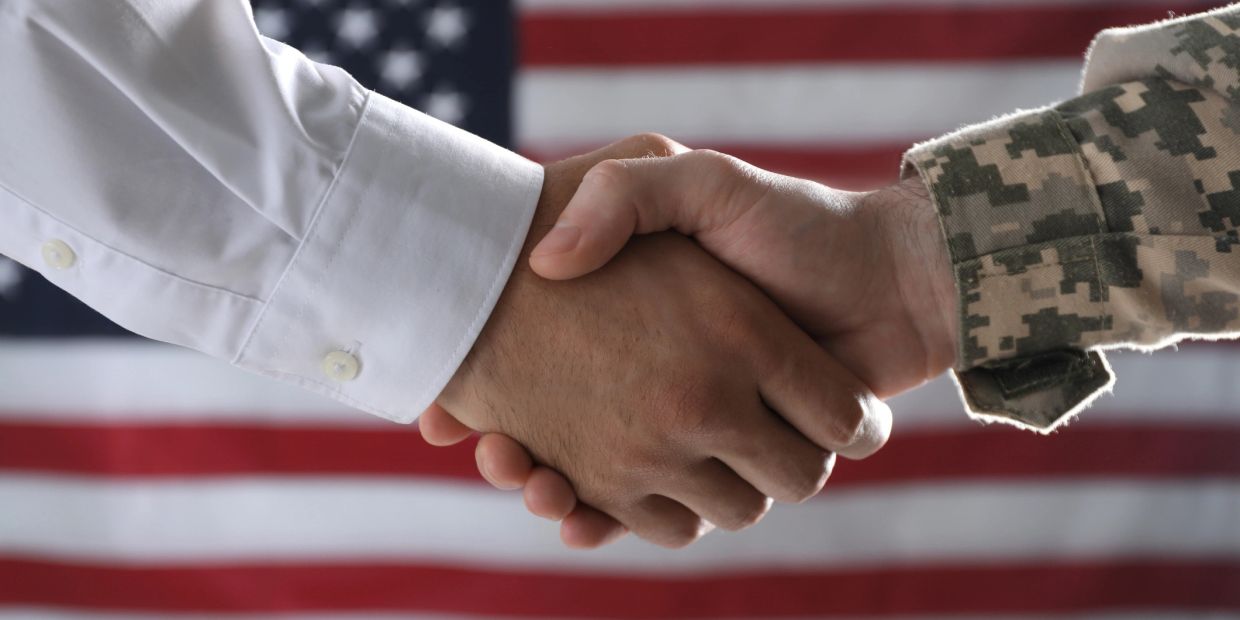 Handshake between a civilian and a soldier with an American flag backdrop.