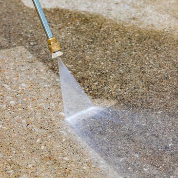 Pressure washing a dirty concrete surface to clean it.