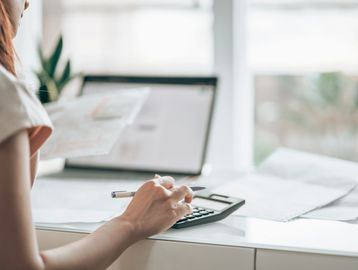 Person using a calculator at a desk with papers and a laptop.