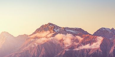 Sunset-lit mountain range with clouds hovering over peaks.