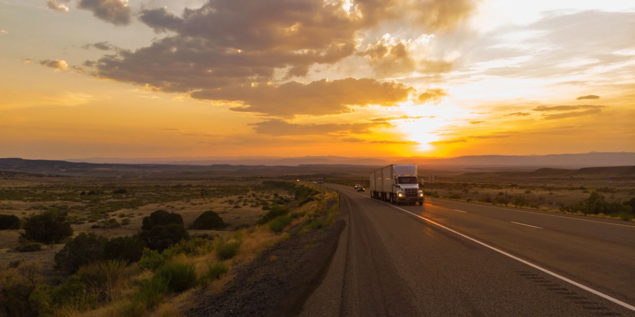 Truck driving on a highway during sunset in a desert landscape.