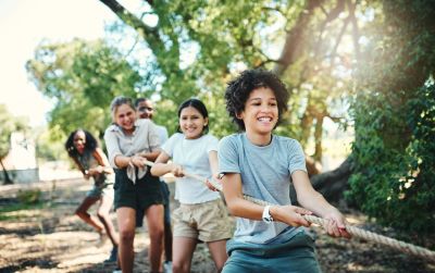 Children joyfully playing tug-of-war outdoors on a sunny day.