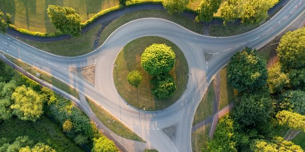 Aerial view of a green roundabout with surrounding trees and roads.