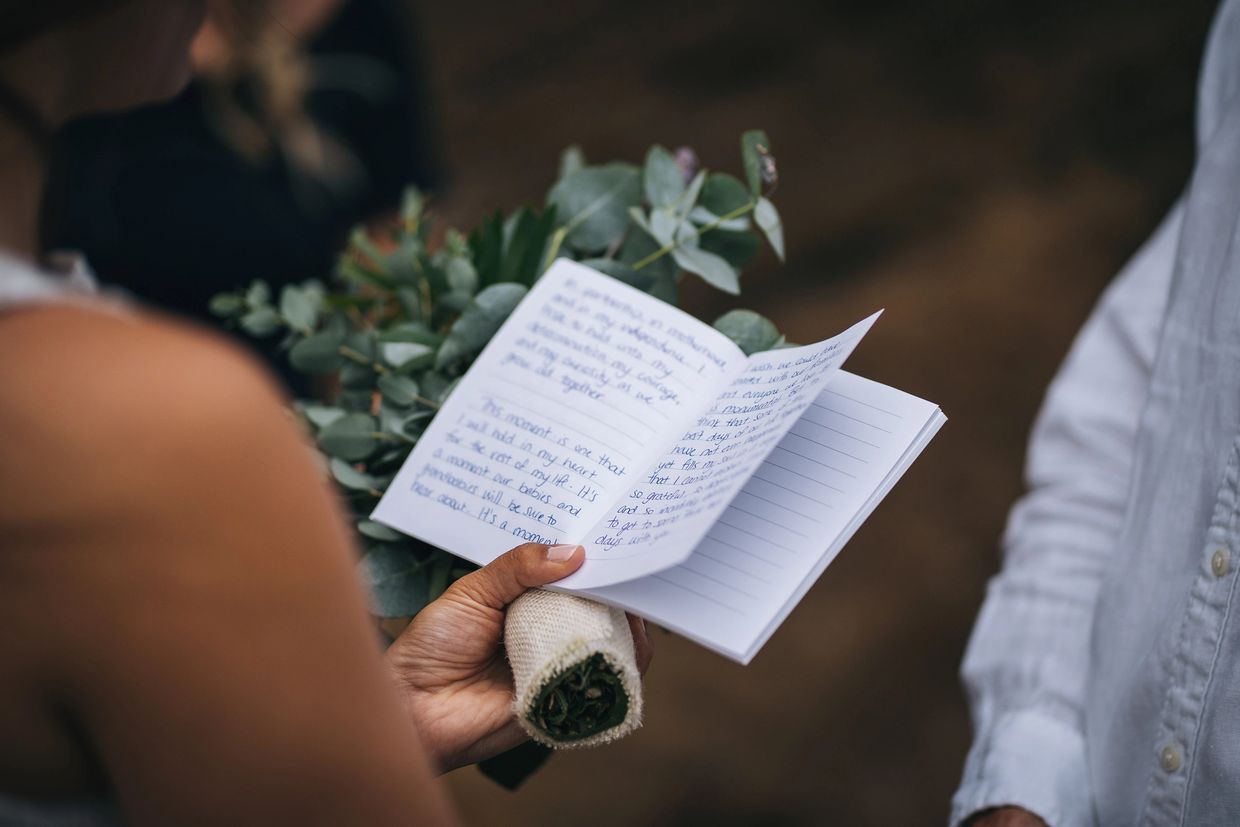Person reading handwritten notes from a small notebook while holding a bouquet.