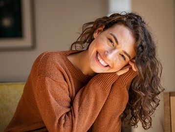 Smiling woman with curly hair in a brown sweater.
