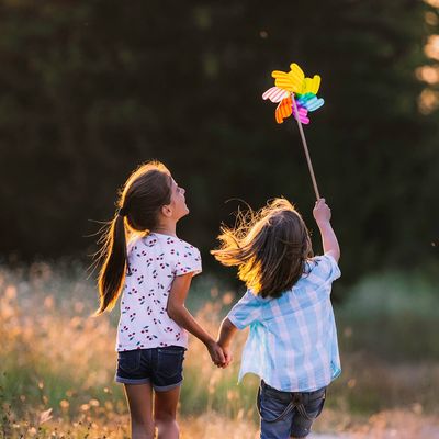 Two kids holding hands with pinwheel in the sunset.