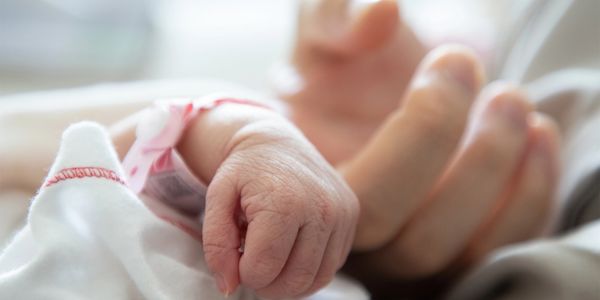 Close-up of a tiny newborn hand gripping an adult finger in the NICU, symbolizing resilience, love.