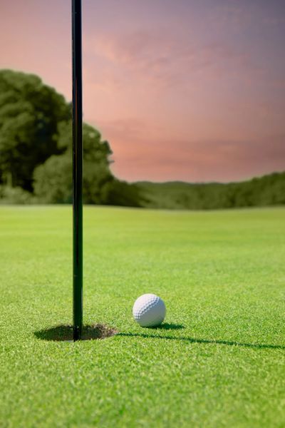 A golf ball near the hole on a green at sunset.