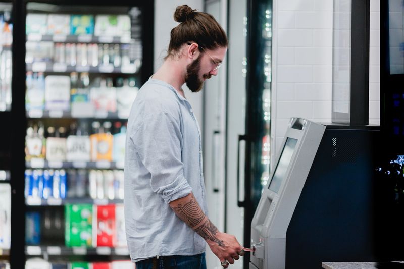 A young man in his 20s is using an ATM Machine at a mini mart.
