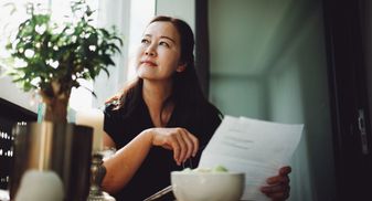 Woman holding papers and looking thoughtfully out a window.
