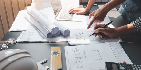 Architects collaborating over blueprints and a laptop at a workspace.