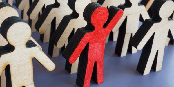 A red wooden figure standing out among natural wood-colored figures.