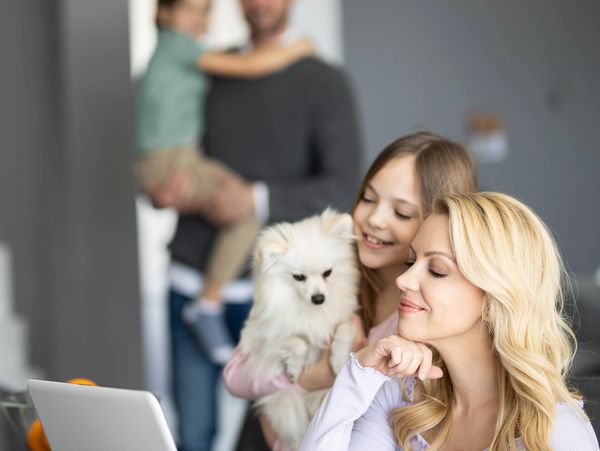 A woman working on a laptop looking for whole life coverage with family and a dog nearby.