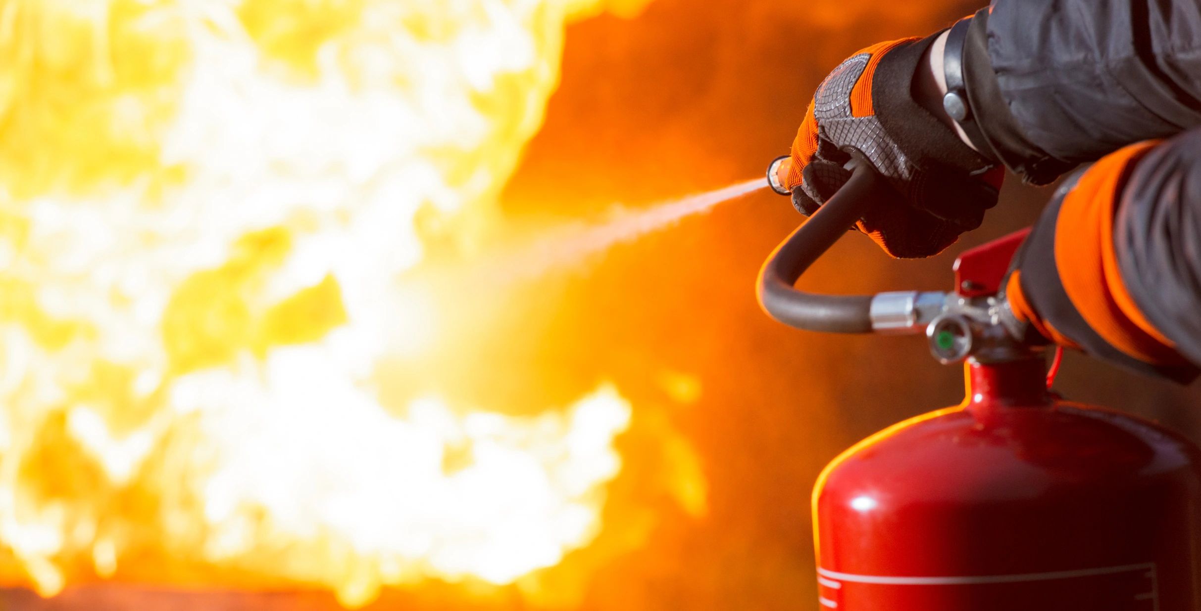 Worker in protective gear using a portable fire extinguisher on a fire