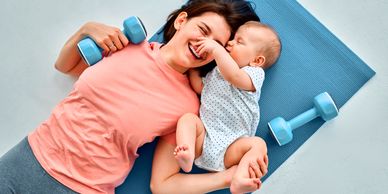 Mother and baby bonding on exercise mat with dumbbells.
