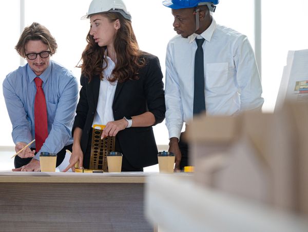 Three engineers discussing plans at a construction site wearing safety helmets.