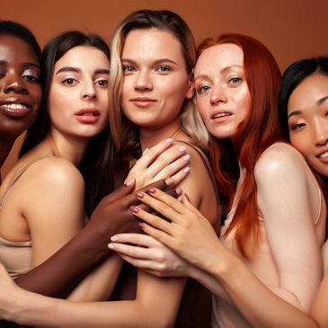Diverse group of five women embracing and smiling against a warm brown background.