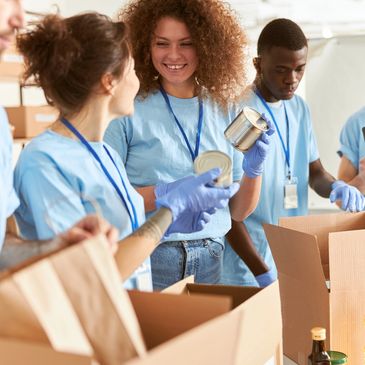 Volunteers in blue shirts packing canned food into boxes at a community center.