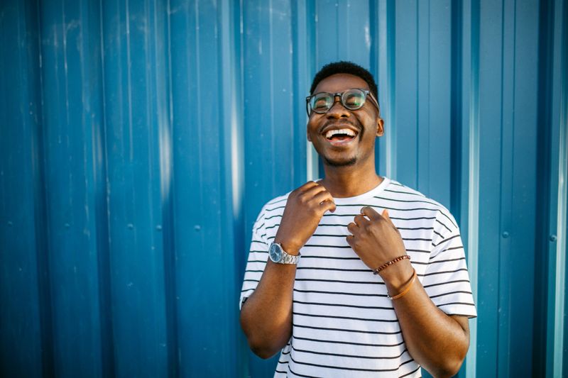 Portrait of young, handsome, smiling, black man with eyeglasses on blue door background, laughing.