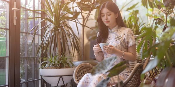 Woman in traditional dress enjoying tea surrounded by plants.