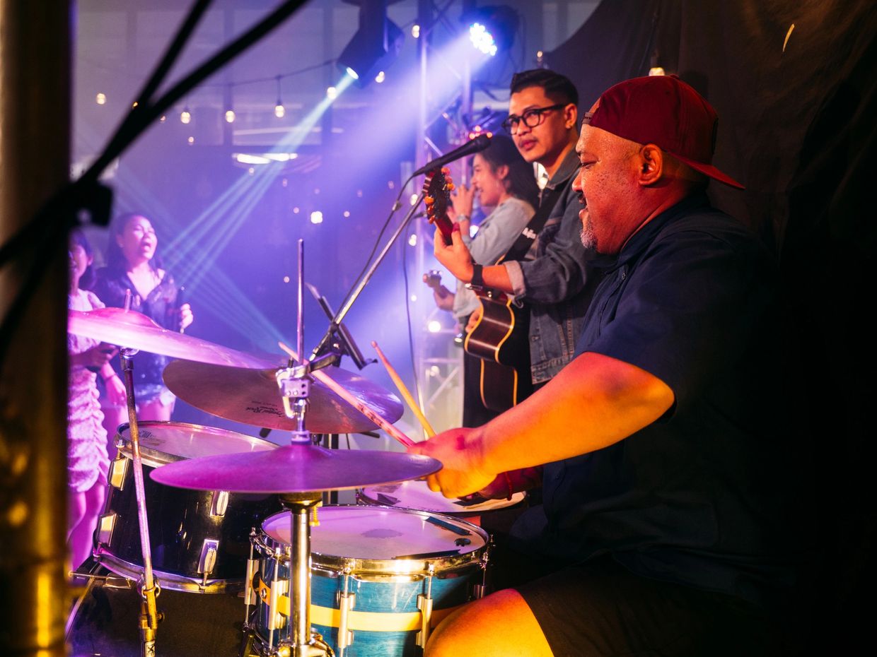Band performing live with focused drummer in foreground.