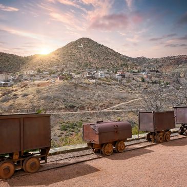 Old mining carts on tracks with a mountainous backdrop at sunset.
