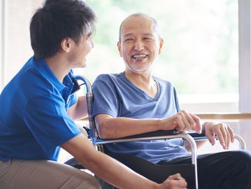 A caregiver smiling and chatting with an elderly man in a wheelchair.