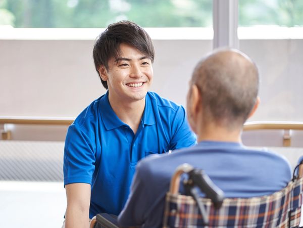 Young caregiver smiling and interacting with elderly man in wheelchair.