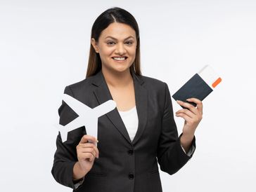 Smiling woman holding a paper airplane and passport with tickets.