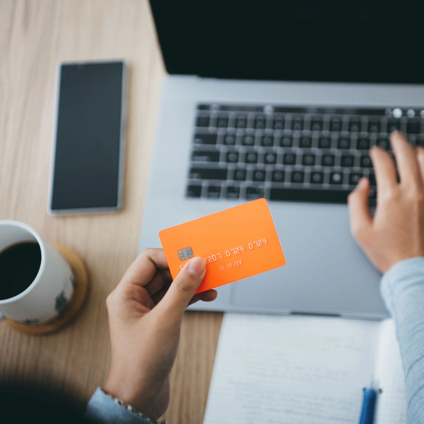 Person holding an orange credit card near a laptop keyboard.