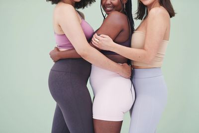 Three diverse women in activewear embracing each other warmly.