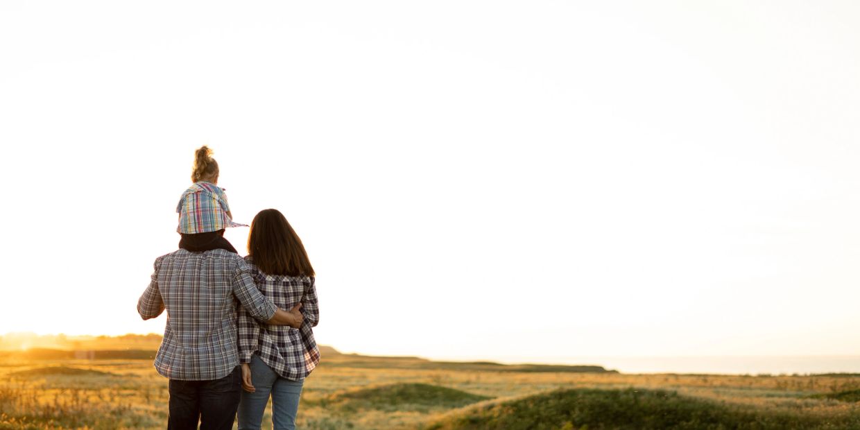 Family of three enjoying sunset on a grassy hill.