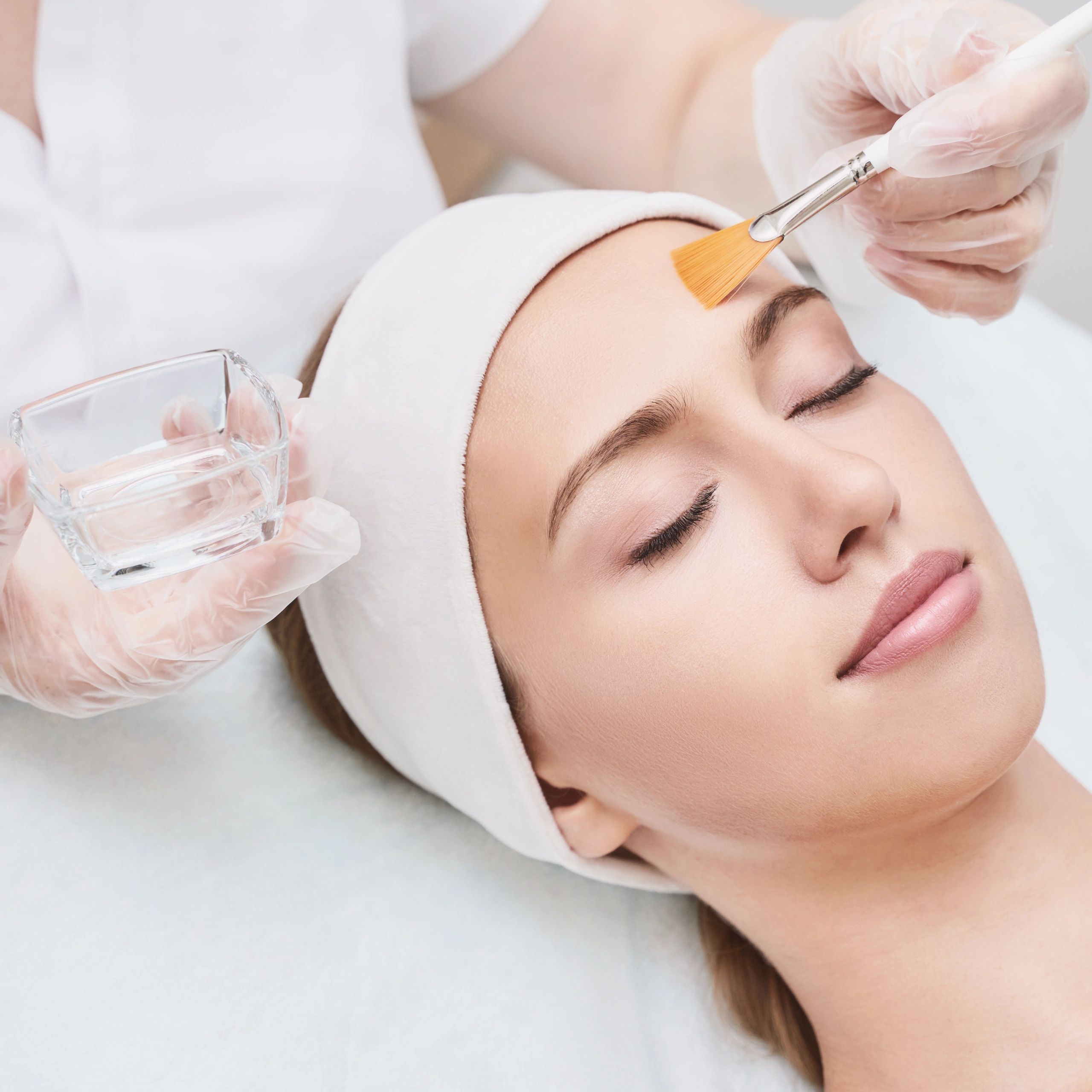 Woman receiving a gentle facial treatment with a brush and water.