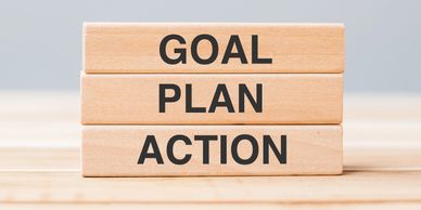 Wooden blocks with words Goal, Plan, and Action stacked on a wooden surface.
