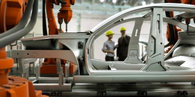 Robotic arms assembling a car frame with two engineers discussing in the background.