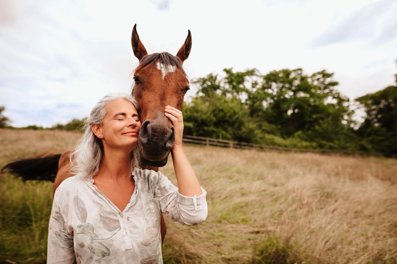 Beautiful mature woman enjoying with closed eyes her brown arabian mare in the free nature. Selective focus. Slightly grain. Part of a series.