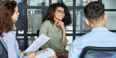 Three people engaged in a meeting with one woman speaking.